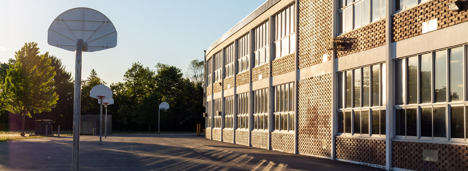 Schoolyard with basketball court and school building exterior in the sunny evening.